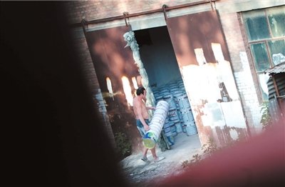 　在位于房山窦店镇西安庄村的假漆制造窝点内，制假工人将假多乐士漆桶从隔壁取回，准备灌注厂房车间内制好的假漆。