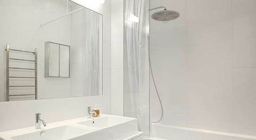 从墙壁到地面，从洁具到配件，纯白色的卫浴间如一尘不染的禁地。白色的浴室柜肩负着整个空间的收纳工作，上方安装双人洗面盆让这个卫浴间小而实用