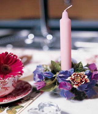 根据烛托的大小，用紫色、粉色的鲜花做一个大小相同的花环，将烛托置入其中，再插上一枝白色蜡烛，点燃蜡烛，雅致花朵更加迷人