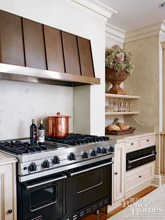 黑色的灶具和泛着古典光晕的铜质抽油烟机是厨房里的焦点，旁边的家具简洁又不失细节设计